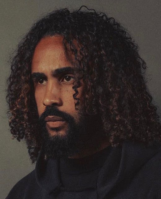 Esse traz MUITO estilo e presença também, viu irmão?
Aqui o destaque vai pros cachos longos, sim, comprimento longo, bem definidos e com movimento natural.
As laterais podem ser mais baixas ou até com fade suave, pra valorizar ainda mais o volume no topo, caso você queira!